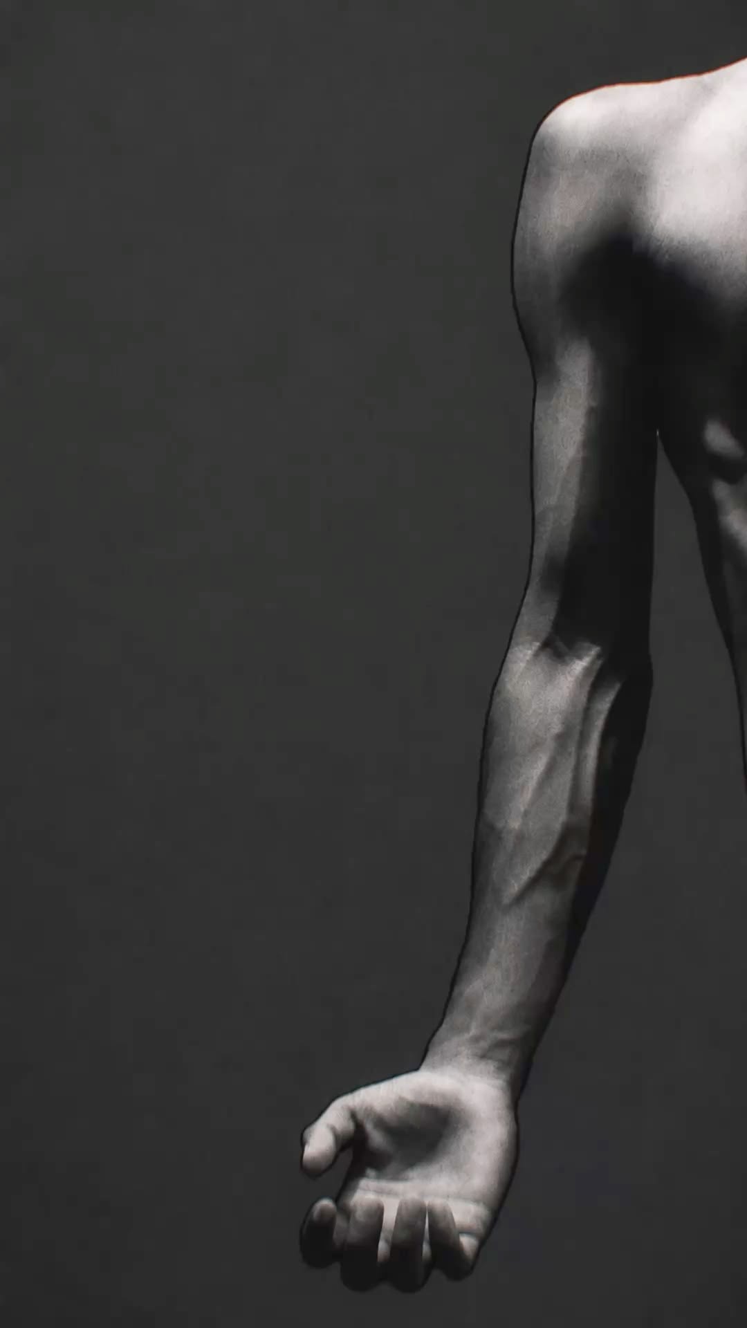 A black and white photograph of a bare shoulder and arm against a dark grey wall, the veins of the forearm standing out and the hand hanging loose and half open.